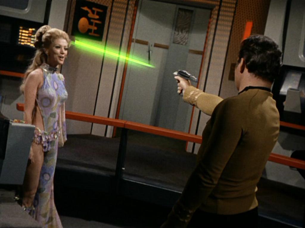Woman in revealing costume dodges a phaser beam being fired by Kirk