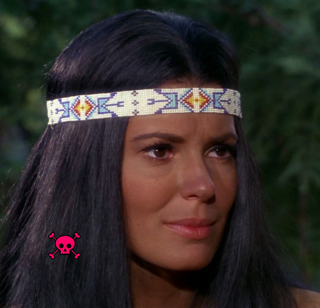 Woman with dark makeup on and long black hair, wearing a beaded headband