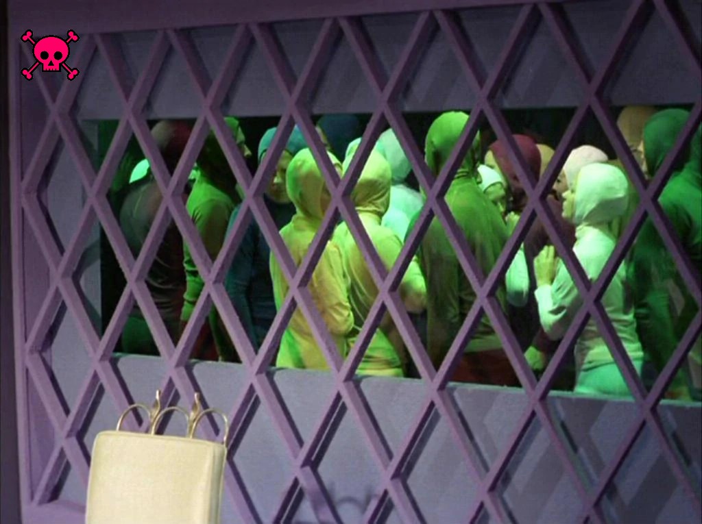 Through a window with diamond-shaped panes, we see a huge crowd of people in green jumpsuits standing literally shoulder-to-shoulder