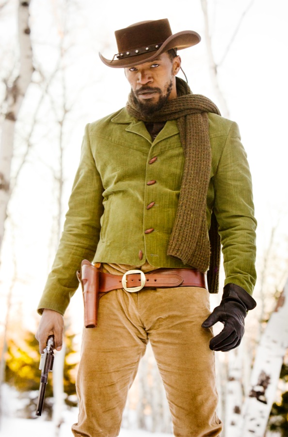 A black man wearing a brown cowboy hat, green long-sleeved jacket, black gloves, a right-handed leather holster, and tan pants.