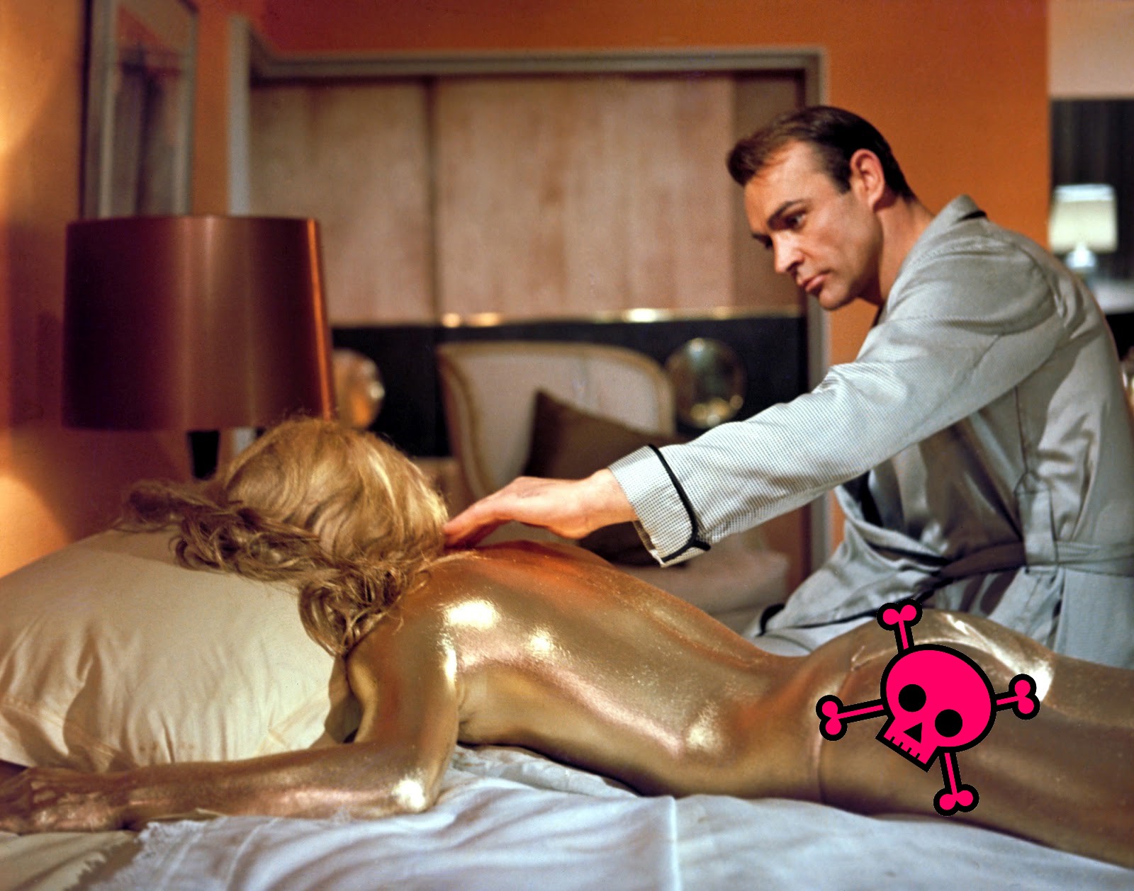 Sean Connery reaches towards a nude woman lying facedown, with every inch of skin covered in gold paint. The site's pink-skull logo is covering her ass.