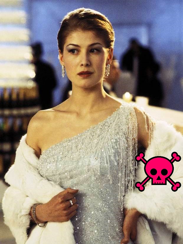 Rosamund Pike wearing diamond earrings, a sparkly off-shoulder white dress, and a white fur stole. Pink skull-and-crossbones logo is on one of her sleeves.