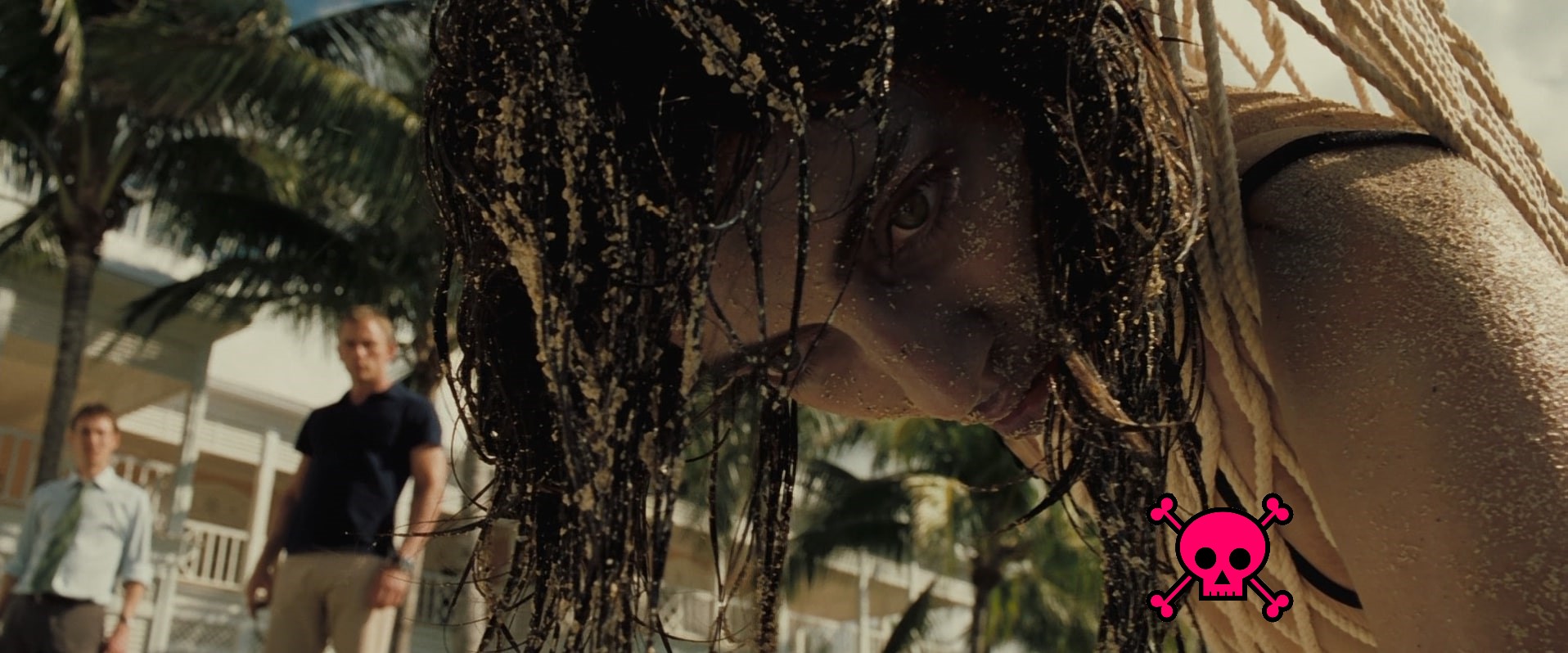 Foreground: woman's corpse dangling from a hammock with sand all over her hair and face (and the site's logo hiding her cleavage). Background: Daniel Craig looks on.