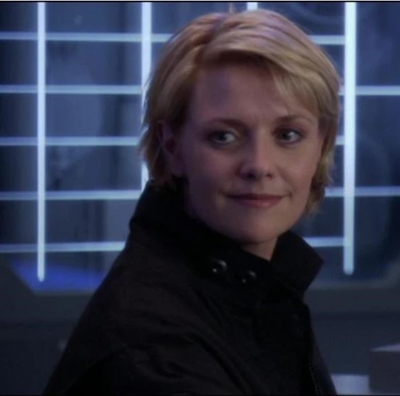 Amanda Tapping with short blonde hair and a black uniform on