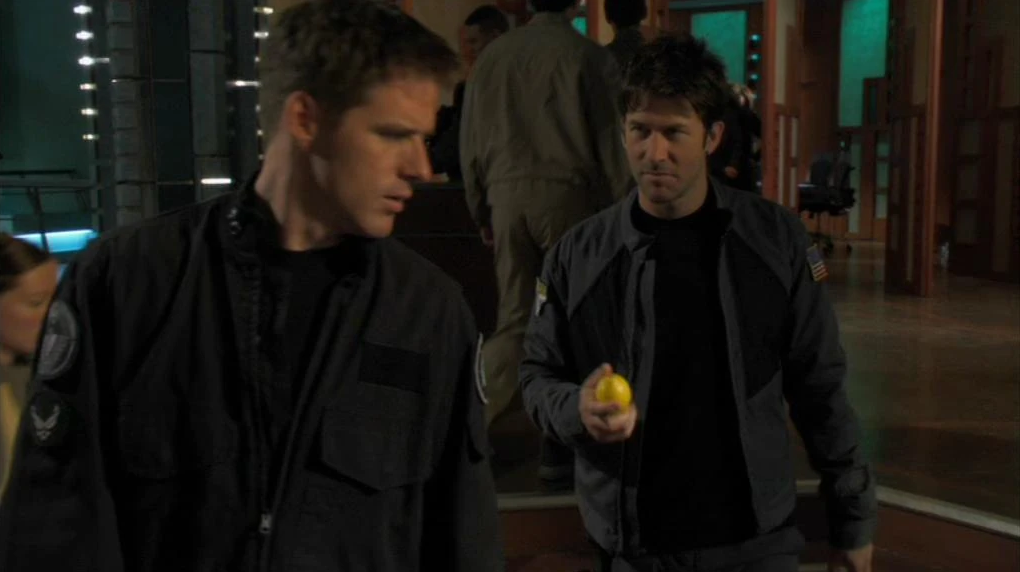 Description: 2 brunet men in Air Force Uniforms. One is handing a lemon to the other.