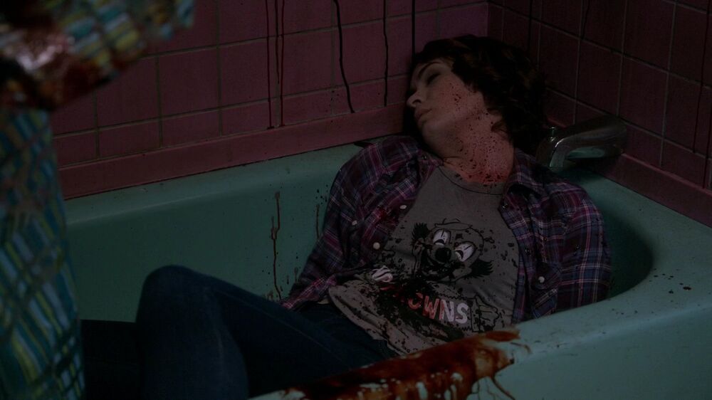 a redheaded woman, wearing a plaid button-down over a T-shirt, lying bloodied in a bathtub